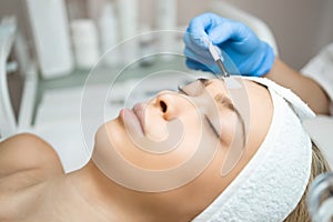 Beautician applies a transparent moisturizing mask to the woman`s face using a brush. Preparation for ultrasonic cleansing