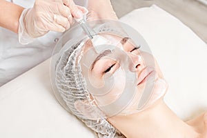 Beautician applies vitamins cream mask on woman face for rehydrate face skin in beauty salon