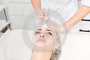 Beautician applies vitamins cream mask on woman face for rehydrate face skin in beauty salon