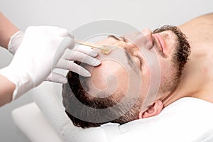 Beautician applies wax between male eyebrows