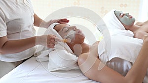 Beautician applying clay facial mask on young Asian woman face