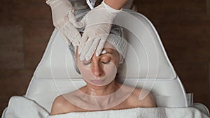 Beautician applying cleansing foam on females face