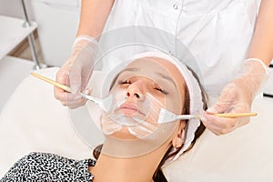 Beautician applying cosmetic cream mask on woman face for rejuvenation, procedure in beauty salon