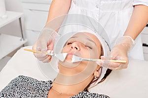 Beautician applying cosmetic cream mask on woman face for rejuvenation, procedure in beauty salon