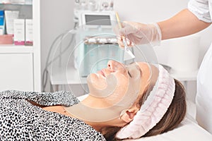 Beautician applying cosmetic cream mask on woman face for rejuvenation, procedure in beauty salon