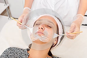 Beautician applying cosmetic cream mask on woman face for rejuvenation, procedure in beauty salon