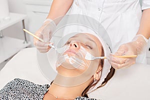 Beautician applying cosmetic cream mask on woman face for rejuvenation, procedure in beauty salon