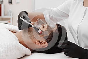 Beautician applying cosmetic mask on man`s face in spa salon.