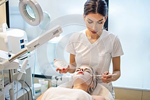 Beautician applying enzymatic peeling on woman& x27;s face in spa. photo