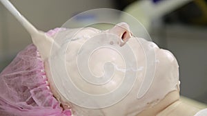 Beautician applying facial mask on a woman face, cleaning skin treatment