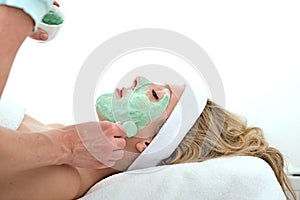 Beautician applying green facial mask on a woman.