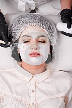 Beautician applying mask on woman face with cosmetic brush.