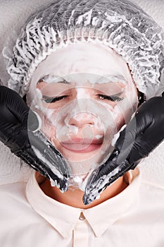 Beautician applying mask on young woman face.