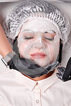 Beautician applying mask on young woman face.