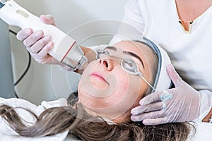 Beautician applying radio frequency microneedling handpiece to a woman`s face for skin tightening treatments at a beauty clinic photo