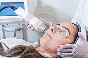 Beautician applying radio frequency microneedling handpiece to a woman`s face for skin tightening treatments at a beauty clinic