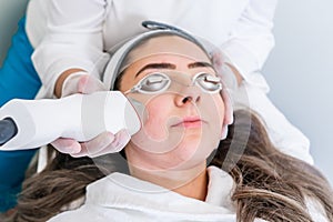 Beautician applying radio frequency microneedling handpiece to a woman`s face for skin tightening treatments at a beauty clinic photo
