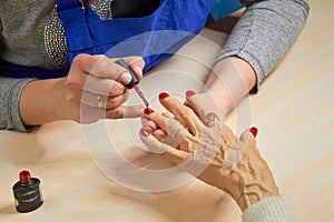 Beautician applying red varnish to woman nails.