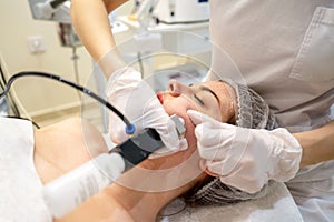 Beautician applying rejuvenation treatment on young woman face in beauty salon.