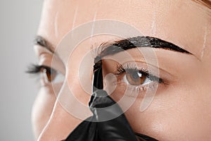 Beautician applying tint during eyebrows correction procedure on grey, closeup