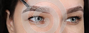 Beautician applying tint during eyebrows correction procedure on light grey background, closeup