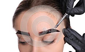 Beautician applying tint during eyebrows correction procedure on white background, closeup