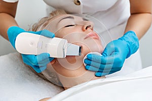 A beautician in blue gloves does an ultrasound cleaning of a woman& x27;s face. Cleansing and rejuvenating procedure in a