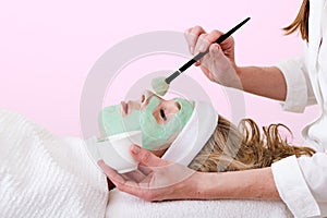 Beautician brushing green facial mask on a woman.