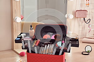 Beautician case with professional makeup products and tools on wooden table