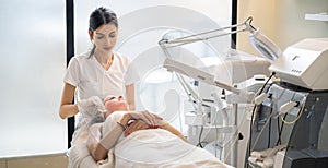 Beautician cleaning the skin of a young woman using cotton discs, finishing her facial treatment in beauty salon