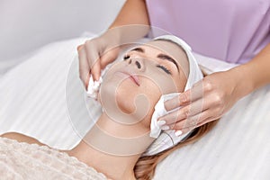 beautician cleanses skin of beautiful woman with sponge.