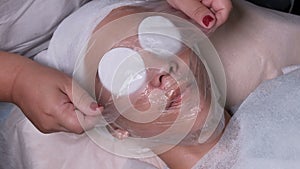 Beautician covers the face of a teenager boy with a transparent film. Closeup of a woman`s hands. Male client gets facial cosmetol