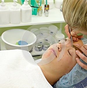 Beautician depilating a woman with tweezers