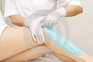 Beautician depilating young womans legs with liquid sugar in spa center. depilation of legs with turquoise