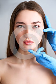 Beautician doctor`s hands in gloves touching face of attractive woman. Fashion blonde model after cosmetic treatment