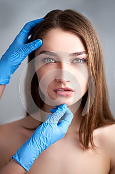 Beautician doctor`s hands in gloves touching face of attractive woman. Fashion blonde model after cosmetic treatment