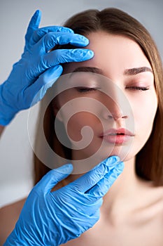 Beautician doctor`s hands in gloves touching face of attractive woman. Fashion blonde model after cosmetic treatment