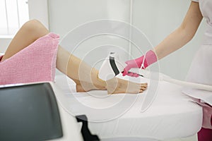 Beautician doing epilation on beautiful girl`s leg in medical center. Female receiving laser light hair removal