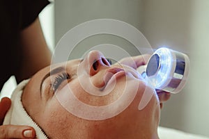 Beautician doing led light therapy to woman with problematic skin in SPA