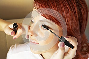 Beautician is doing make-up to red-haired girl photo