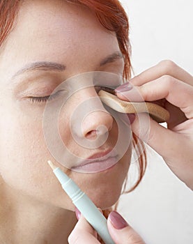 Beautician is doing make-up to red-haired girl photo