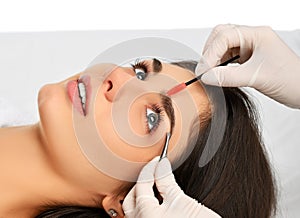 Beautician doing permanent eyebrows makeup. Closeup composition of beautiful woman face with thick brows In beauty salon