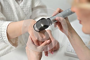 Beautician examine the skin on the female hand with a dermatoscope