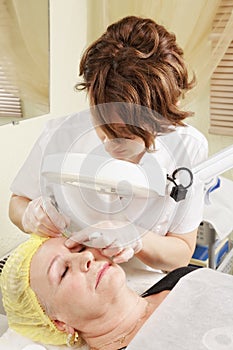 Beautician at eyebrows tweezing procedure