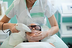 Beautician giving laser epilation treatment to young woman's fac