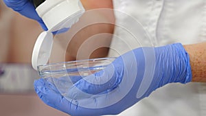 Beautician in gloves squeezes face mask into glass bowl for subsequent application to client face. Cosmetologist