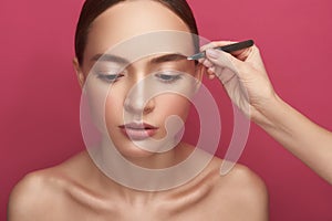 Beautician hand plucking lady eyebrows with tweezers