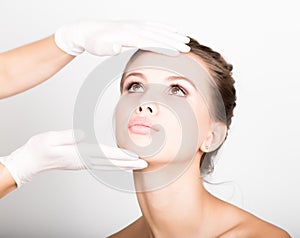 Beautician hand`s examining beautiful young female face.