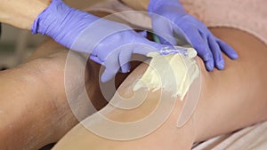 Beautician hands in a blue rubber glove remov unwanted leg hair with shugaring.