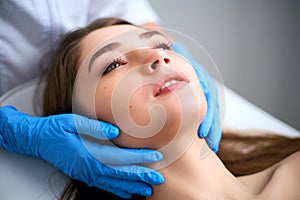 Beautician hands in gloves touching face of attractive woman. Facial Beauty. Beautiful young female with soft smooth